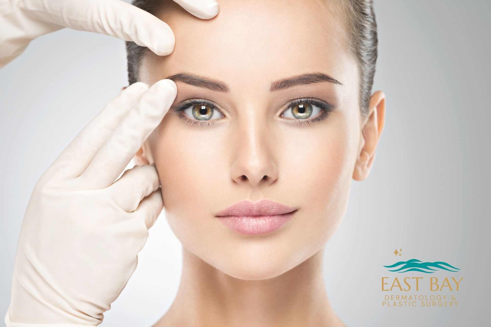 East Bay LP (4) A person with clear skin is examined by gloved hands near the face, with the logo for East Bay Dermatology & Plastic Surgery in the lower right corner.