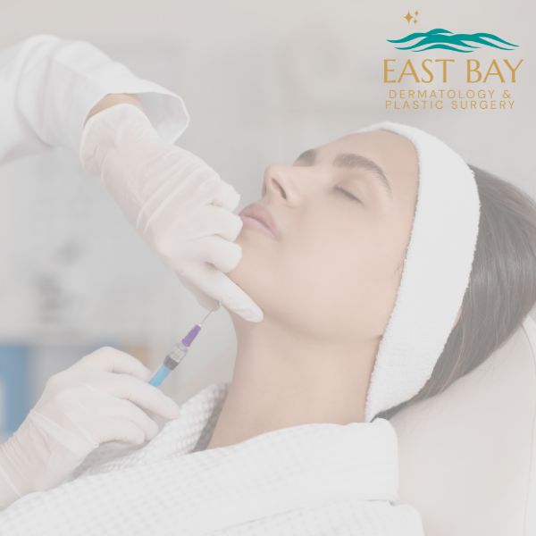 A woman with a headband receives a Kybella for double chin injection in her chin from a gloved medical professional; East Bay Dermatology & Plastic Surgery logo is visible.