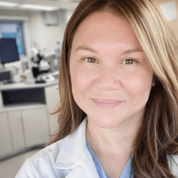 A woman in a white lab coat stands in a laboratory, smiling at the camera. Laboratory equipment and computers are visible in the background, reflecting the expertise and dedication of our providers.