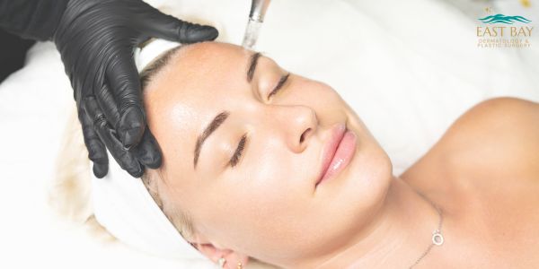 Person receiving a facial skin treatment with a handheld device, while wearing a white headband; a gloved hand holds their head steady.